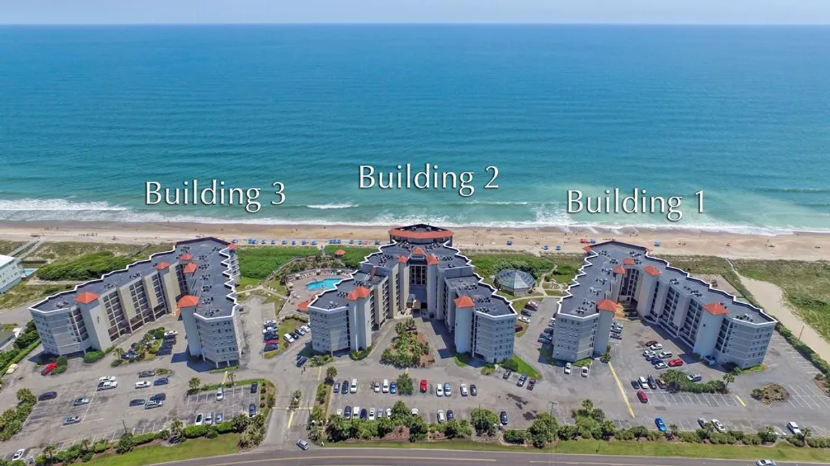 A sweeping view of the property’s three buildings, a spacious swimming pool, and the beautiful ocean in the background. The image highlights the proximity to water activities and relaxation zones, connecting with the narrative of swimming, sunbathing, and easy access to the beach for paddleboarding or volleyball.
