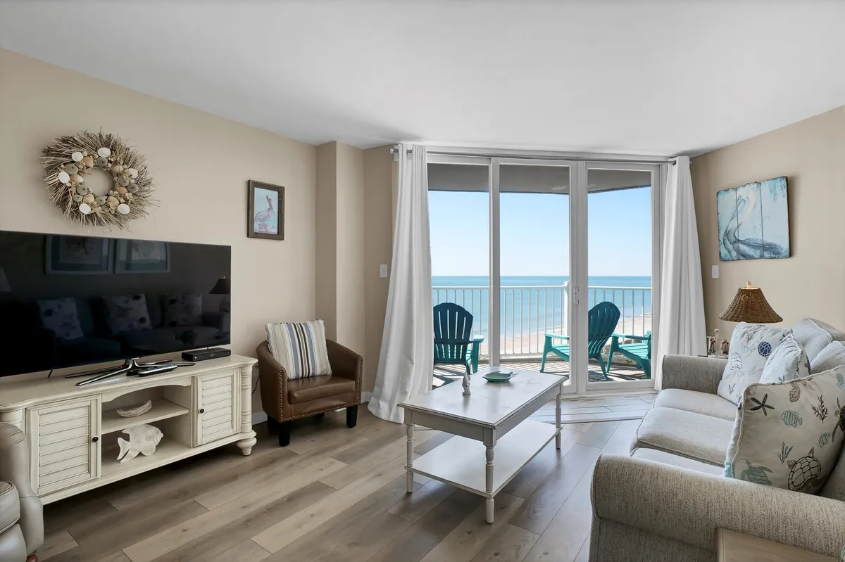 A comfortable living space with a plush sofa facing large windows that frame the sparkling Atlantic. Decor accents like a wreath and TV unit set a relaxed tone, while the ample seating makes it clear this is a place for socializing and unwinding with loved ones.