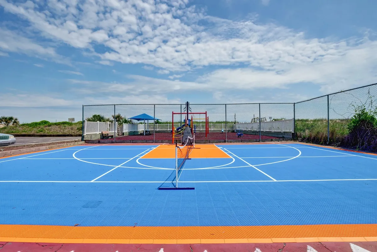 An outdoor recreational area with a basketball court, tennis net, and playground equipment, surrounded by greenery. The lively scene encourages active breaks and connects guests to the community and natural surroundings.