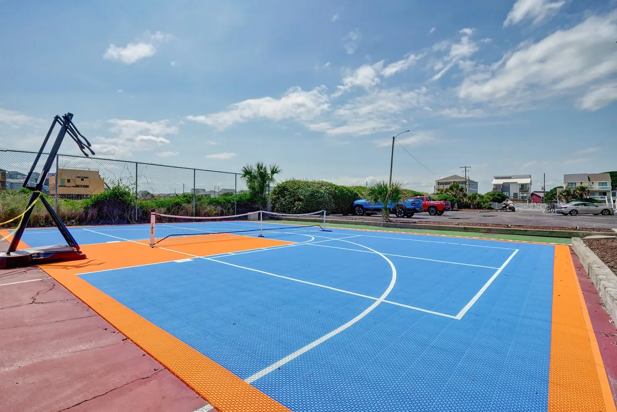 This exterior image features a vibrant basketball hoop and a colorful court surrounded by green foliage. The space is clearly set up for active sports, with ample room for group games or friendly competition. The scene is lively and inviting, encouraging communal play and outdoor fun.