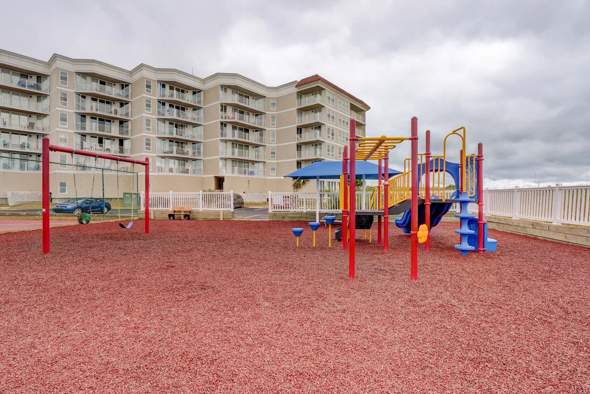 A vibrant outdoor playground with swings and other equipment, set on a colorful surface with apartment buildings in the background. The mood is playful and inviting, echoing the family-friendly aspect of the resort.