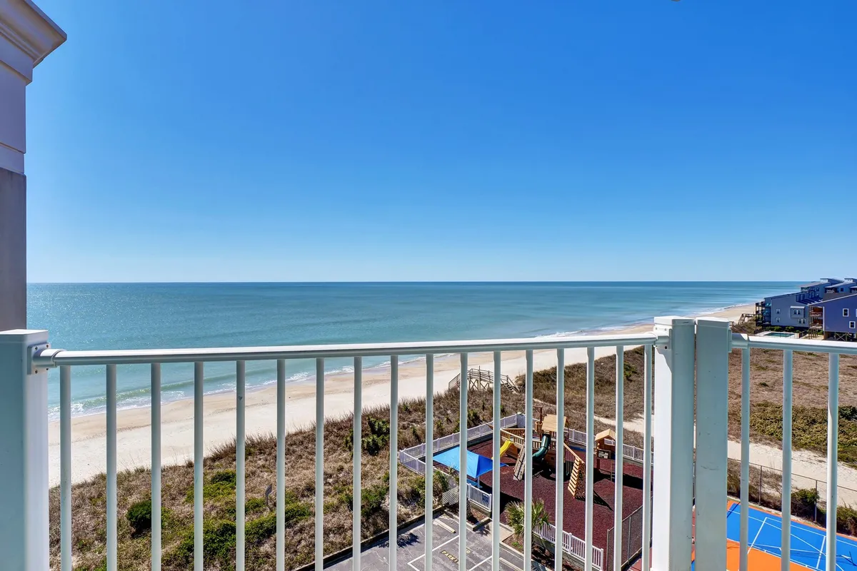 A panoramic view including the beach, ocean, a playground area, and nearby building structures. The relaxed beachfront setting offers both natural beauty and amenities for leisurely strolls and quiet escapes along the shore.
