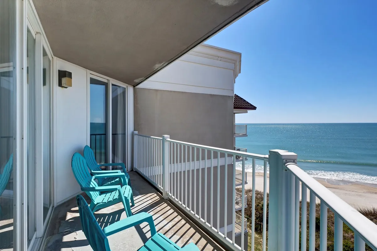 An exterior view featuring a balcony with comfortable chairs positioned to take in a sweeping ocean vista. The tranquil ambiance is perfect for enjoying a drink while listening to the rhythmic waves below.
