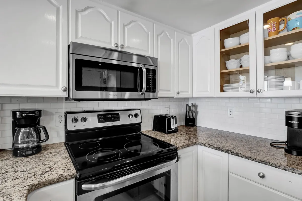This image features a kitchen equipped with stainless steel appliances, a striking granite countertop, and open shelving displaying dishware. The scene feels warm and inviting, suggesting activity such as baking or entertaining, and the open layout hints at a social connection to adjacent living spaces.