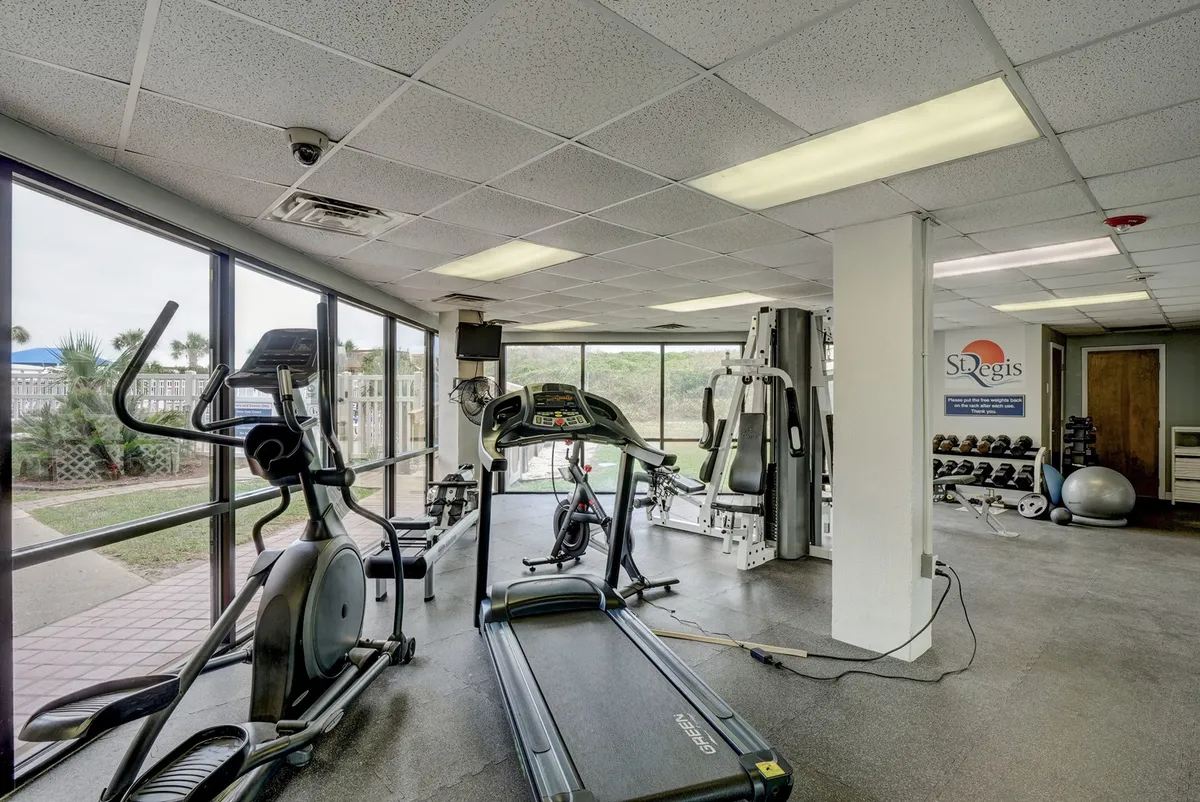 A modern fitness center filled with natural light, featuring treadmills, elliptical machines, weight stations, and large windows that bring in expansive views. It conveys an energetic and motivational environment for wellness and restorative breaks.