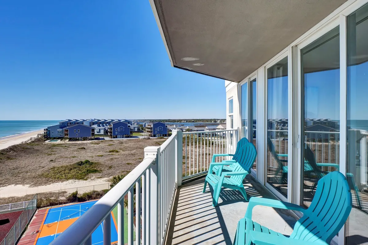 A tranquil exterior shot showing a private balcony with inviting blue chairs overlooking an expansive ocean view. The scene evokes peace and relaxation, with the gentle waves visible below and a perfect vantage point for sunrises or sunsets.