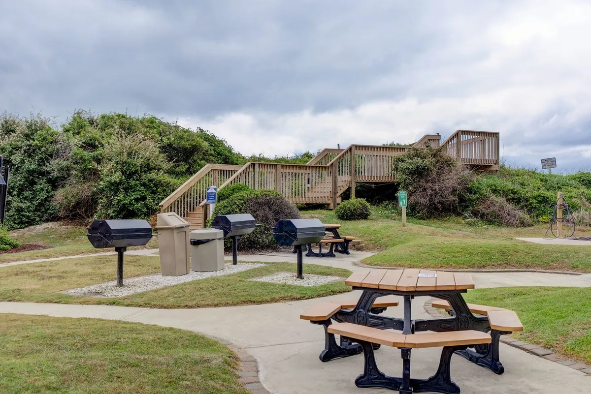 An inviting outdoor area with several picnic tables and charcoal grills, ideal for barbecuing or group meals. The setting is relaxed, open-air, and conducive to socializing, echoing the section's mention of communal grilling and outdoor dining after a day of activities.