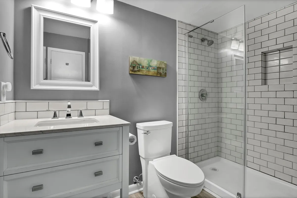A bright and refreshing bathroom featuring a vanity with sink, a glass-enclosed shower, a framed mirror, and tasteful coastal artwork. The space feels clean and tranquil, perfect for unwinding after a day by the sea.